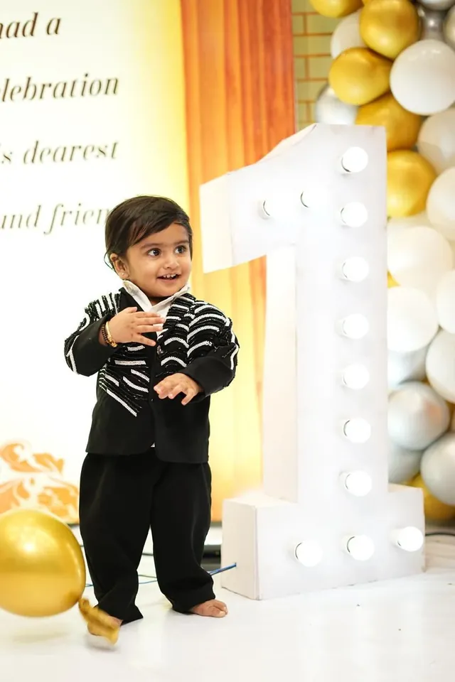 A young boy in a black embroidered suit at a birthday celebration