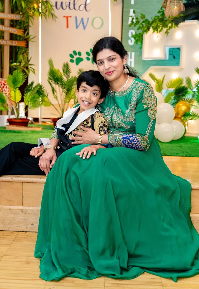 A mother in an emerald-green embroidered dress seated with her son