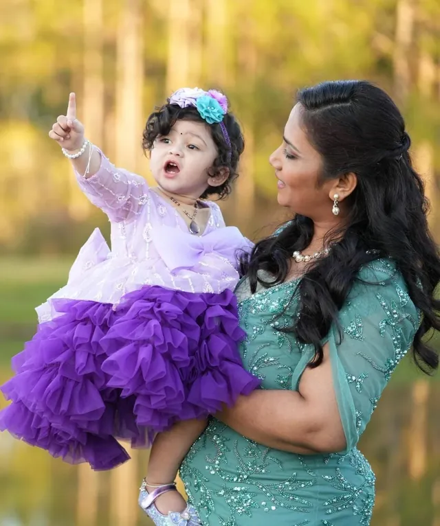 A mother holding her daughter in a purple ruffled dress outdoors