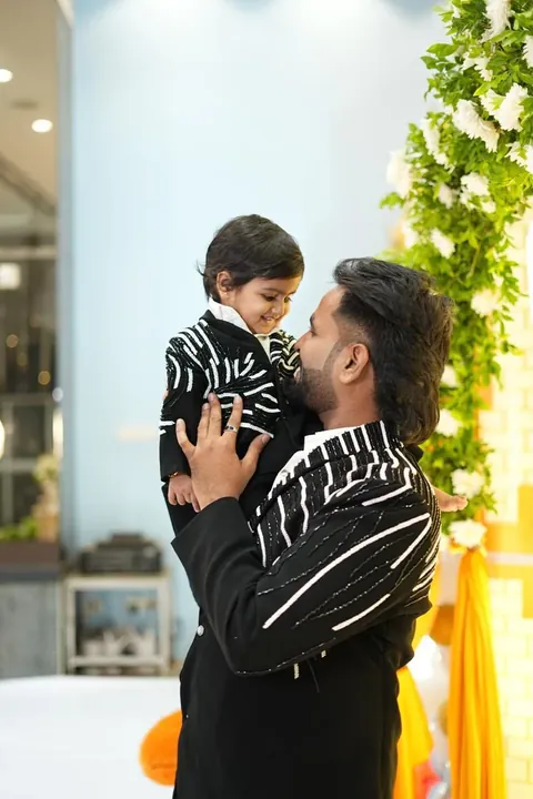 A father lifting his child, both in black jackets with white stripe beadwork